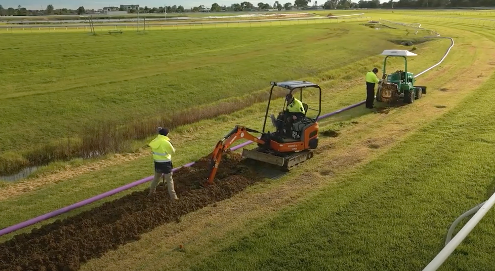 a small excavator digs a trench for a a purple pipe.